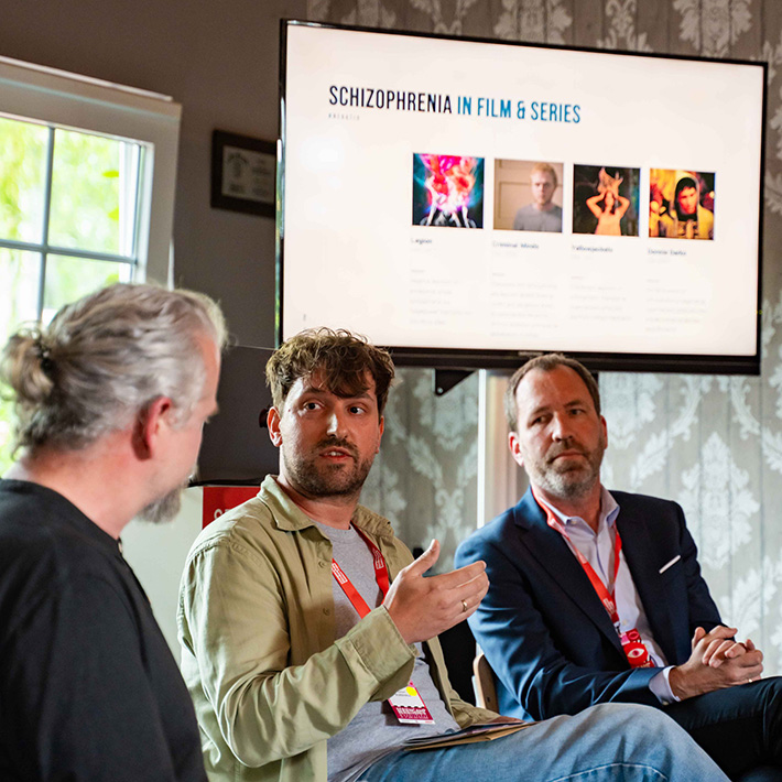 3 Speaker bei der Podiumsdiskussion vor Bildschirm